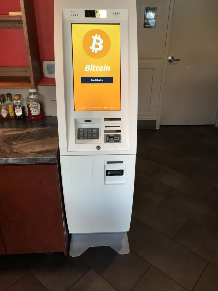 Bitcoin ATM kiosk with yellow display screen showing Bitcoin logo and Buy Bitcoin button in an indoor commercial space