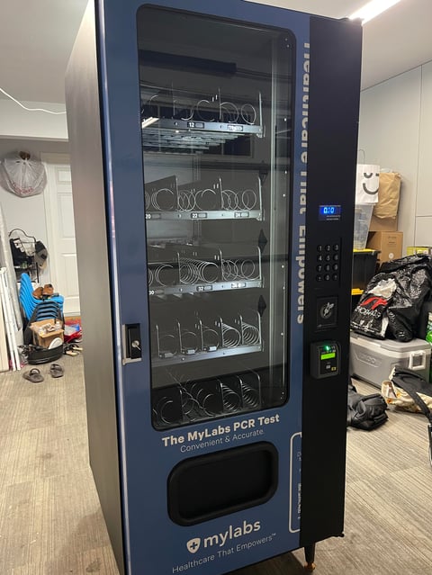 MyLabs PCR Test vending machine with multiple shelves displaying test kits in a bright indoor facility