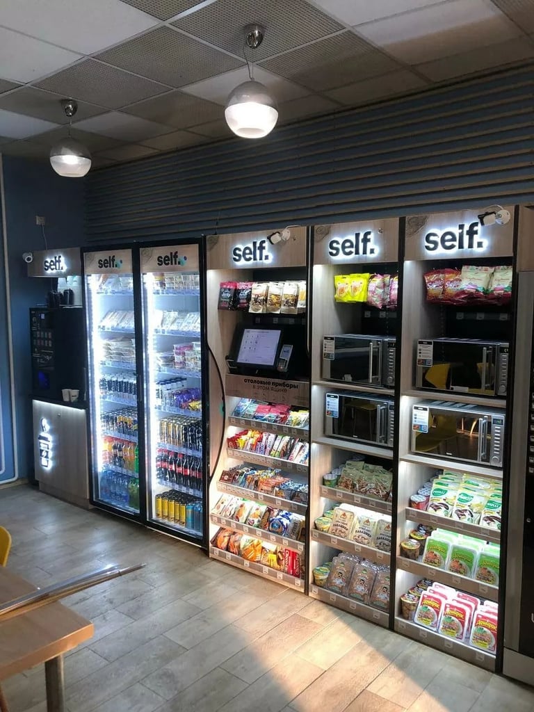 Row of self-service vending machines with snacks and beverages in a convenience store with modern lighting and blue striped walls