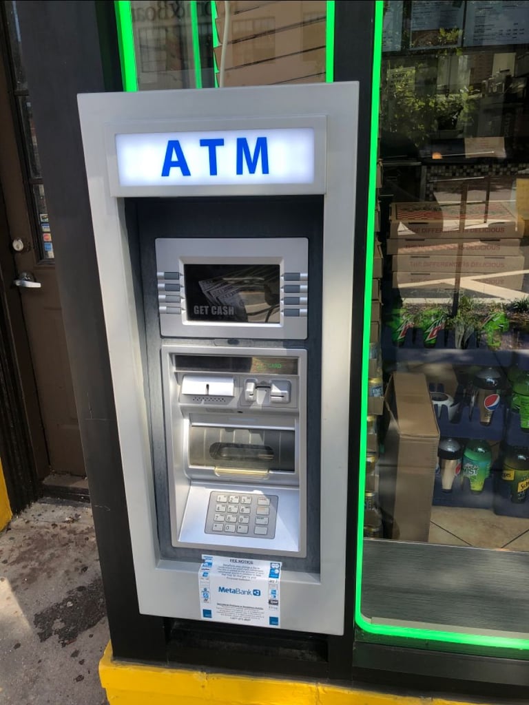 ATM machine with white frame and blue signage mounted against dark wall with green neon lighting accents
