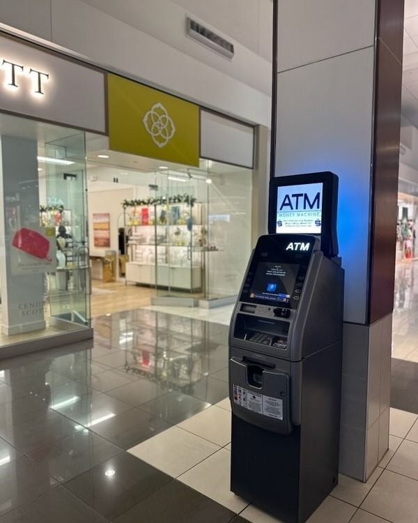 Black ATM machine in a modern mall hallway with storefronts and bright lighting in the background