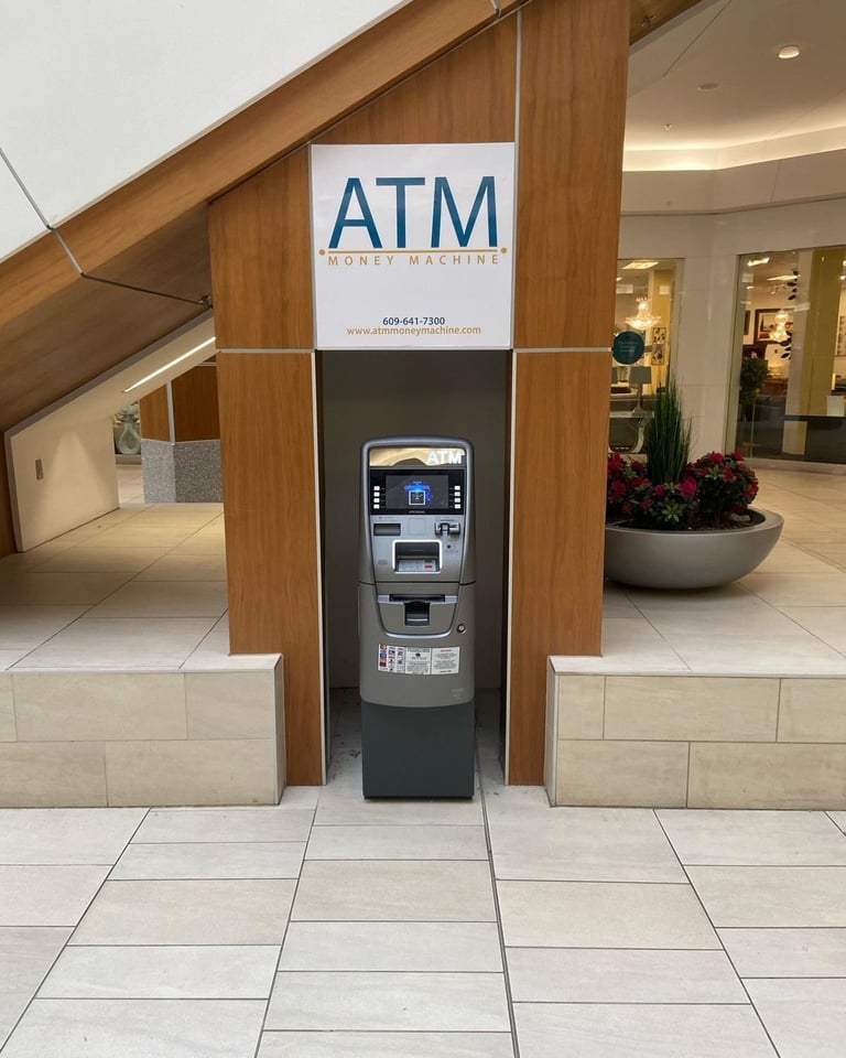 ATM money machine in modern mall with wood and stone kiosk structure, white tile flooring, and storefront in background