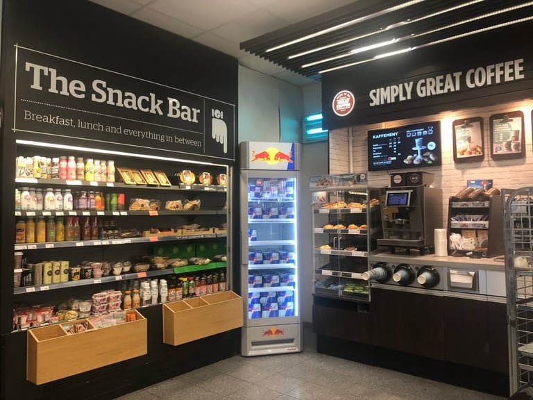 Interior of a café with The Snack Bar section featuring shelves of packaged snacks and a beverage cooler, and Simply Great Coffee counter on the right