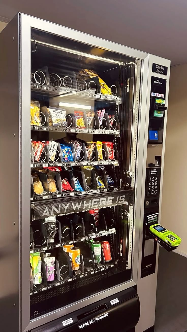 A vending machine stocked with snacks and beverages including chips, candies, and drinks with illuminated shelves and a payment keypad on the side